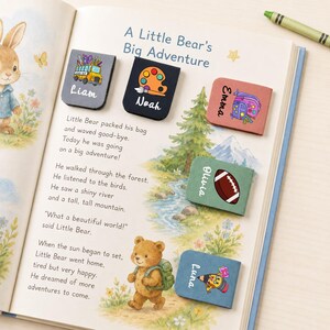 May include: A children's book titled "A Little Bear's Big Adventure" with colorful magnetic bookmarks. The bookmarks feature illustrations of a school bus, paint palette, backpack, football, and a pencil, each with a child's name.