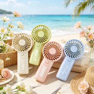May include: Four handheld portable fans in pastel colours of cream, light green, peach, and light blue. Each fan features a circular head with a protective grille, a handle with a power button, and a wrist strap. The names Willow, Molly, Cooper, and Marley are printed in white on the handles.