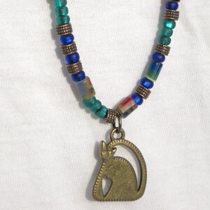 May include: A necklace with a brass cat pendant. The necklace is made of blue and green glass beads.