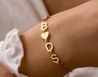 May include: A gold bracelet with the letters B, D, and S, linked by a heart-shaped charm. The bracelet is a fine chain design. The letters are in a simple font. The bracelet is worn on a wrist.