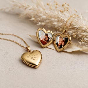 Może przedstawiać: Dwa złote medaliony w kształcie serca na delikatnych łańcuszkach. Jeden medalion jest zamknięty i wygrawerowany napisem "Love you, Mom" oraz małym serduszkiem. Drugi medalion jest otwarty, ukazując wewnątrz dwa osobne kolorowe zdjęcia pary.