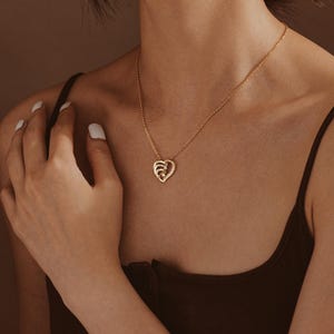 K&ouml;nnte beinhalten: Eine goldene Halskette mit einem herzf&ouml;rmigen Anh&auml;nger, der mehrere kleinere Herzen enth&auml;lt. Der Anh&auml;nger ist mit kleinen funkelnden Steinen verziert.
