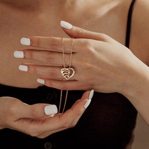 K&ouml;nnte beinhalten: Eine goldene Halskette mit einem herzf&ouml;rmigen Anh&auml;nger und einer zarten Kette. Der Anh&auml;nger hat ein mehrschichtiges Herzdesign mit kleinen funkelnden Steinen.