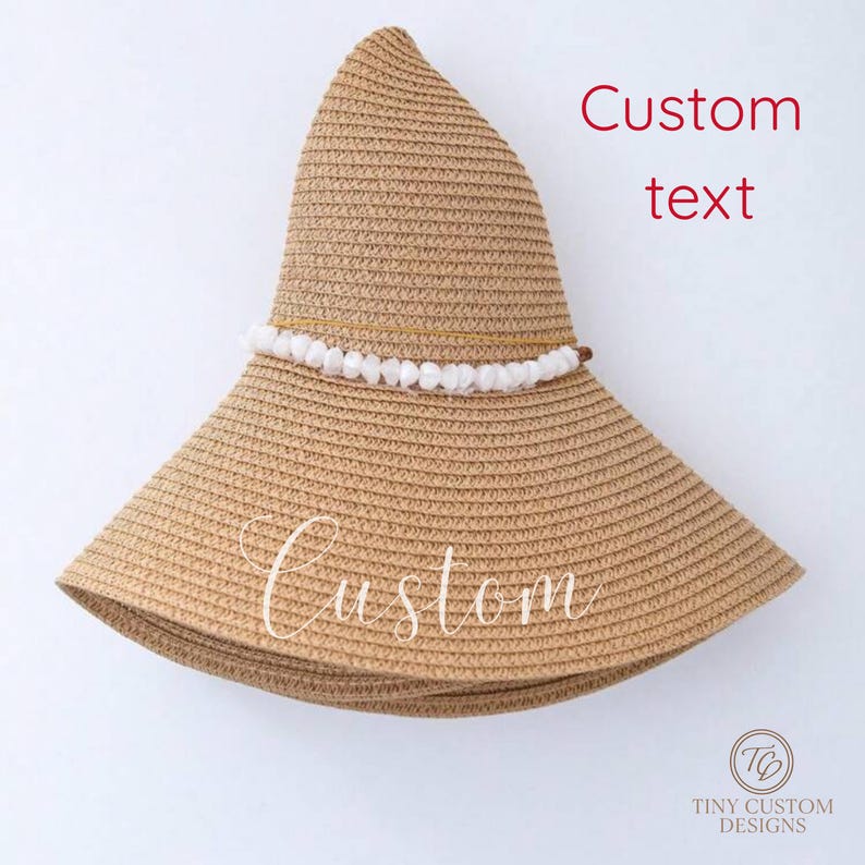 May include: A tan straw sun hat with a wide brim and a decorative band of white beads. The hat has the word "Custom" written on the brim and "Custom text" written on the crown. The hat is from Tiny Custom Designs.