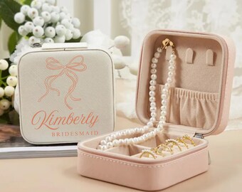 May include: A pink and white jewelry box with a bow and the name Kimberly Bridesmaid printed on the lid. The box is open and has a necklace, earrings, and rings inside.