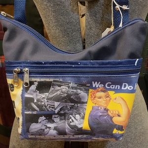 May include: Navy blue shoulder bag with a zipper closure and a strap. The bag features a graphic print of Rosie the Riveter with the text "We Can Do It" and black and white images of women working.