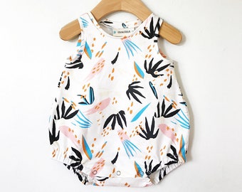 May include: White baby onesie with a colorful abstract print featuring black, blue, orange, and pink shapes. The onesie has a round neckline and snap closures.