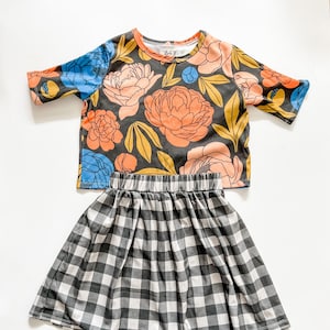 May include: A black and white gingham skirt with a floral print top. The top has a round neckline and short sleeves. The skirt has a wide waistband and a gathered skirt.