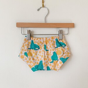 May include: White baby bloomers with a colorful print of teal sea lions on a yellow background.