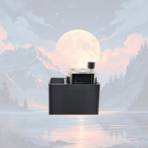 May include: A black rectangular organizer holds two clear glass bottles with black caps. One bottle has a black label. The organizer sits against a backdrop of a full moon, mountains, and water.