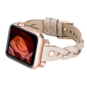 May include: A rose gold Apple Watch with a braided light beige leather band. The band has a rose gold buckle and decorative studs.
