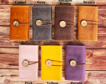 May include: Seven leather wallets in different colors: camel, gray, antique brown, brown, pink, yellow, and purple. Each wallet has a wooden button closure and a leather strap.
