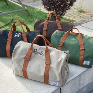 Peut inclure: Quatre sacs de sport en noir, marron, vert et beige, chacun dot&eacute; de poign&eacute;es et de sangles en tissu marron. Le sac noir porte le nom Leli et le sac beige porte le nom Barlow, inscrits respectivement en texte cursif blanc et noir.