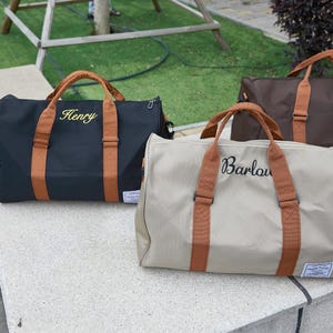 Peut inclure: Trois sacs de voyage en noir, beige et marron, chacun dot&eacute; de poign&eacute;es et de sangles marron clair. Le sac noir est brod&eacute; du nom Henry et le sac beige du nom Barlow. Chaque sac comporte une petite &eacute;tiquette rectangulaire de couleur blanche.