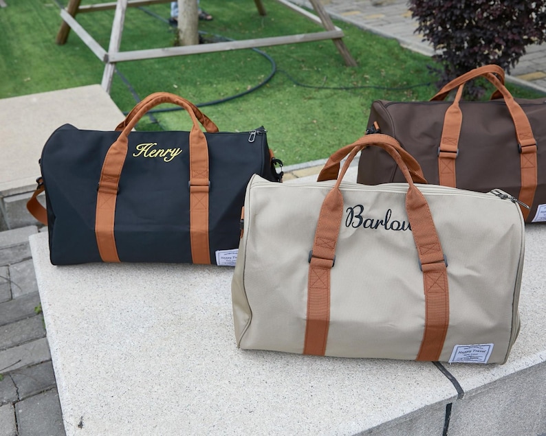 Peut inclure: Trois sacs de voyage en noir, beige et marron, chacun dot&eacute; de poign&eacute;es et de sangles marron clair. Le sac noir est brod&eacute; du nom Henry et le sac beige du nom Barlow. Chaque sac comporte une petite &eacute;tiquette rectangulaire de couleur blanche.