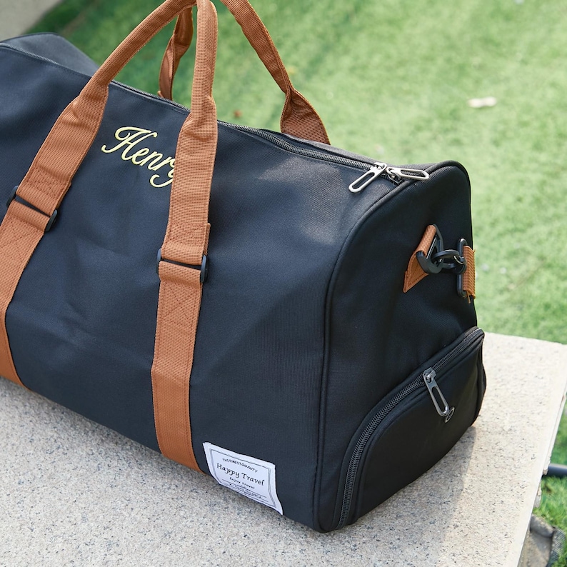Peut inclure: Un sac de sport noir avec des poign&eacute;es et des bordures en tissu beige. Le sac pr&eacute;sente le nom Henry brod&eacute; en lettres dor&eacute;es sur le c&ocirc;t&eacute;, une fermeture &eacute;clair sup&eacute;rieure, un compartiment lat&eacute;ral zipp&eacute; et une &eacute;tiquette blanche Happy Travel.