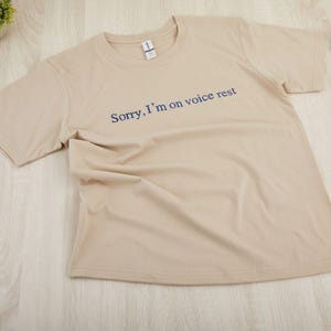 May include: A beige t-shirt with the text "Sorry, I'm on voice rest" printed in blue.
