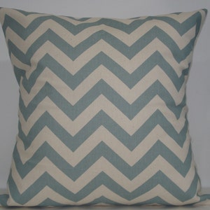 May include: Square cushion with a chevron pattern. The cushion features alternating light blue and off-white zigzags. The cushion is a square shape and appears to be made of a soft fabric.
