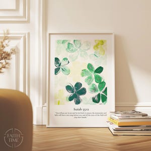 May include: A framed art print featuring a floral design in shades of green and white. The artwork includes the text "Isaiah 55:12" and a related quote. The print is displayed on a wooden floor next to a stack of books.