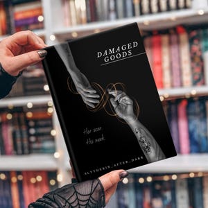May include: A black book cover with the title "DAMAGED GOODS" in white. The cover features a grayscale illustration of two hands reaching for each other, with gold lines connecting them. Text below reads "Her scar. His mark."