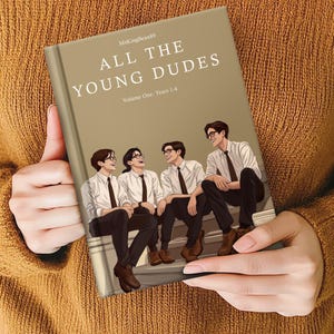 Könnte beinhalten: Eine Person hält ein Buch mit dem Titel "ALL THE YOUNG DUDES". Das Cover zeigt eine Illustration von vier jungen Männern in weißen Hemden, schwarzen Krawatten und Hosen. Der Buchrücken ist in einem gedämpften Grün gehalten, der Hintergrund ist warmbraun.
