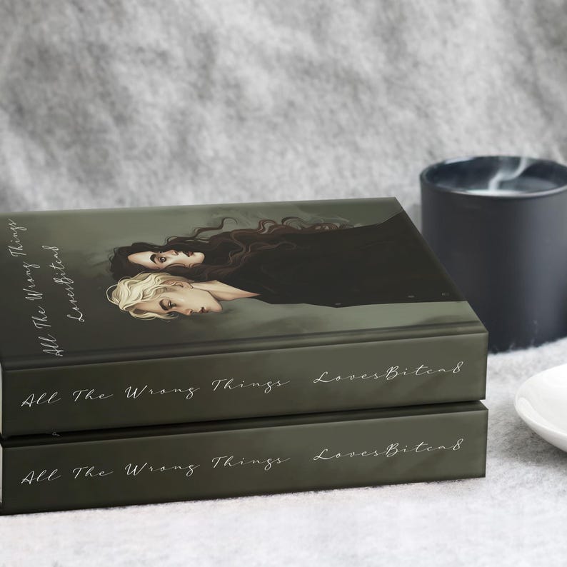 May include: Two hardcover books stacked on top of each other. The book covers are dark green with the title "All The Wrong Things LovesBitend" in white script. The top book features an illustration of two people. A black candle and a white dish are in the background.