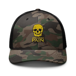 Könnte beinhalten: Eine schwarze und grüne Camouflage-Trucker-Kappe mit einem gelben Totenkopf-Motiv und dem Text "IT'S ONLY PAIN" in Gelb.