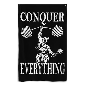 May include: Black wall hanging with the words "CONQUER EVERYTHING" in white, above a white illustration of a weightlifter lifting a barbell. The weightlifter is wearing a helmet and holding a mace.