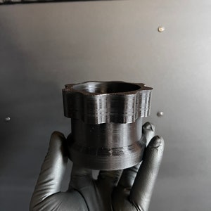 May include: A black plastic 3D printed object with a star-shaped top and a smooth, cylindrical base.