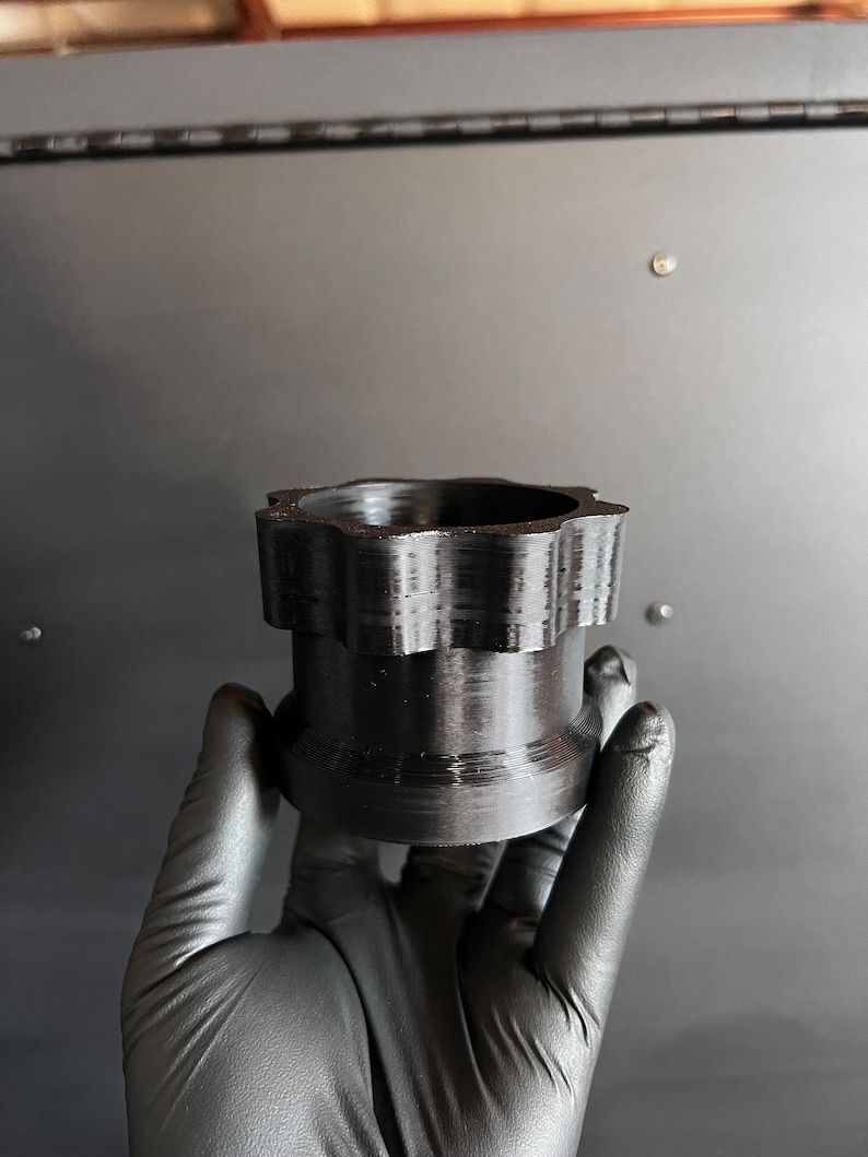May include: A black plastic 3D printed object with a star-shaped top and a smooth, cylindrical base.