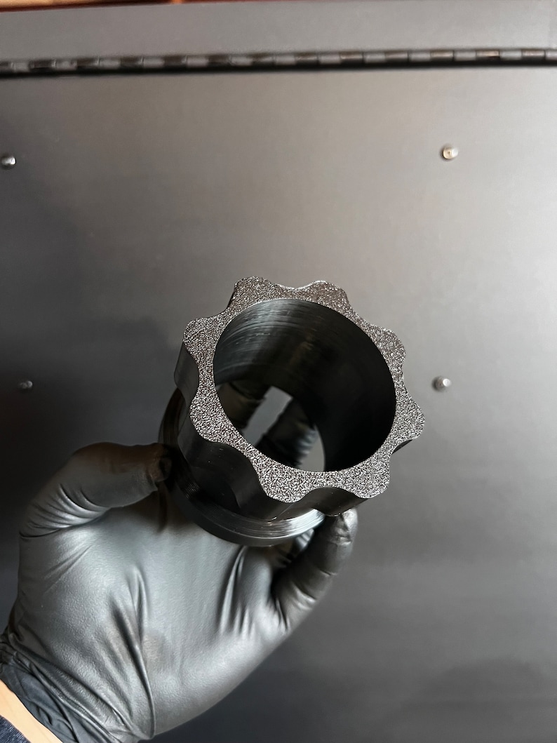 May include: A black plastic gear-shaped object with a textured surface. The object has a large hole in the center.
