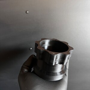 May include: A black plastic 3D printed object with a star-shaped top and a cylindrical base.