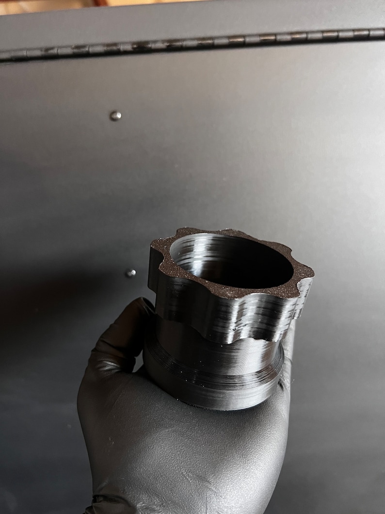 May include: A black plastic 3D printed object with a star-shaped top and a cylindrical base.