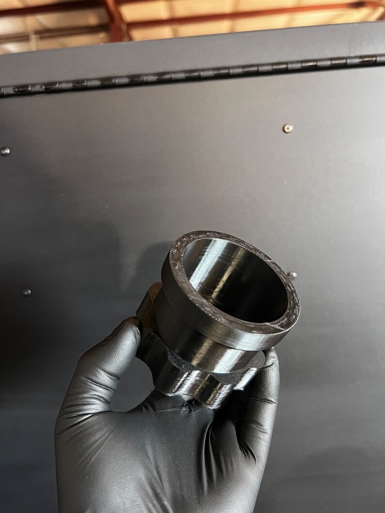 May include: A black plastic 3D printed adapter with a cylindrical shape and a textured surface.