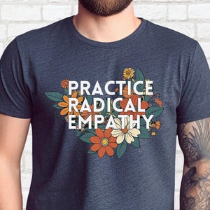 Puede incluir: Una camiseta azul marino con un diseño floral y el texto "PRACTICE RADICAL EMPATHY" en blanco.