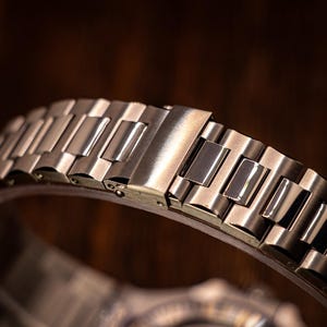 Op de afbeelding: Close-up van een zilveren metalen horlogeband met een sluiting. De band is gemaakt van afzonderlijke schakels die aan elkaar zijn verbonden.