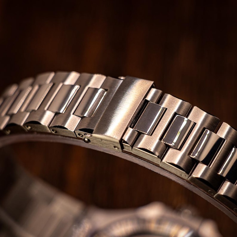 Op de afbeelding: Close-up van een zilveren metalen horlogeband met een sluiting. De band is gemaakt van afzonderlijke schakels die aan elkaar zijn verbonden.