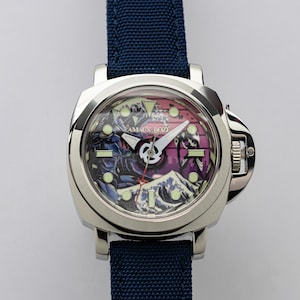 May include: A stainless steel wristwatch with a navy blue fabric strap. The watch face displays a colourful illustration with the text "AMAUX BOZE". The watch has a square face and a silver bezel.