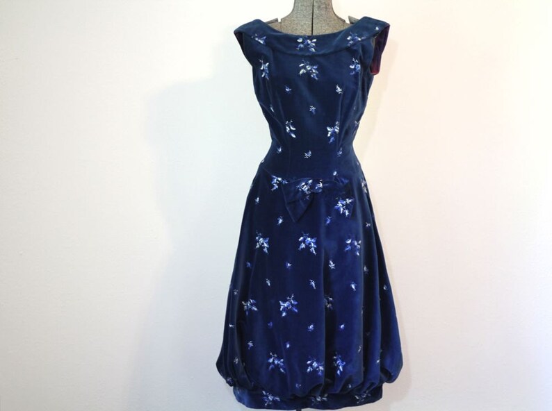 Puede incluir: Un vestido de terciopelo azul marino con estampado floral blanco y un lazo en la cintura.