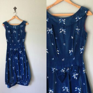 Puede incluir: Un vestido de terciopelo azul con estampado floral blanco y un lazo en la cintura. El vestido es sin mangas y tiene un escote redondo.