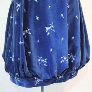 Puede incluir: Una falda de terciopelo azul con un estampado floral blanco. La falda est&aacute; fruncida en la cintura y tiene una silueta amplia y fluida.