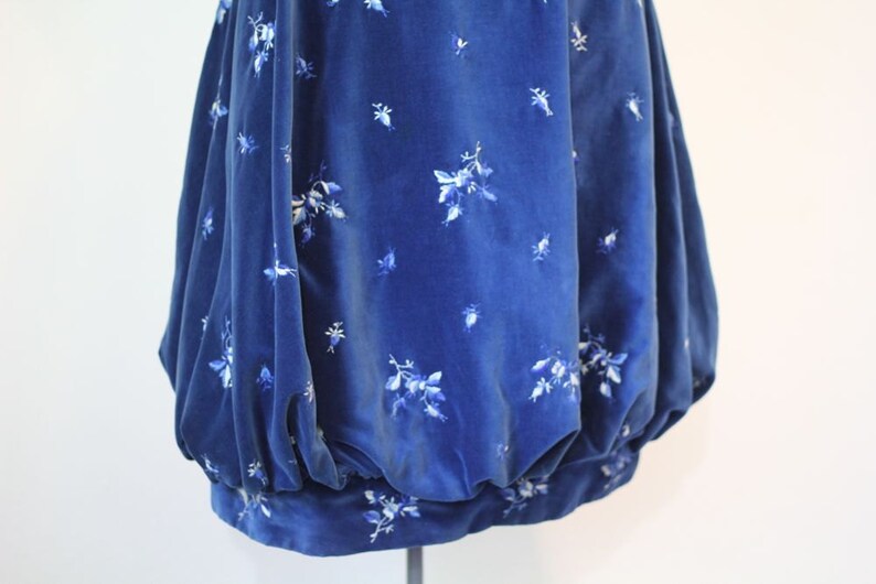 Puede incluir: Una falda de terciopelo azul con un estampado floral blanco. La falda est&aacute; fruncida en la cintura y tiene una silueta amplia y fluida.