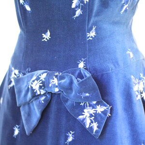 Puede incluir: Un vestido de terciopelo azul con un estampado floral blanco y un gran lazo de terciopelo azul en la cintura.