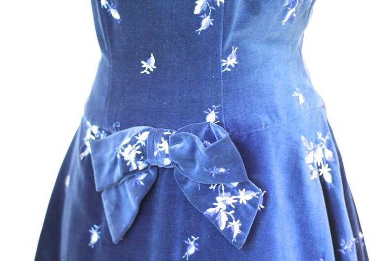 Puede incluir: Un vestido de terciopelo azul con un estampado floral blanco y un gran lazo de terciopelo azul en la cintura.