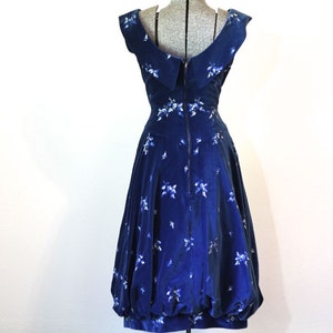 Puede incluir: Un vestido de terciopelo azul con estampado floral blanco y escote de pico. El vestido tiene un corpi&ntilde;o ajustado y una falda completa.