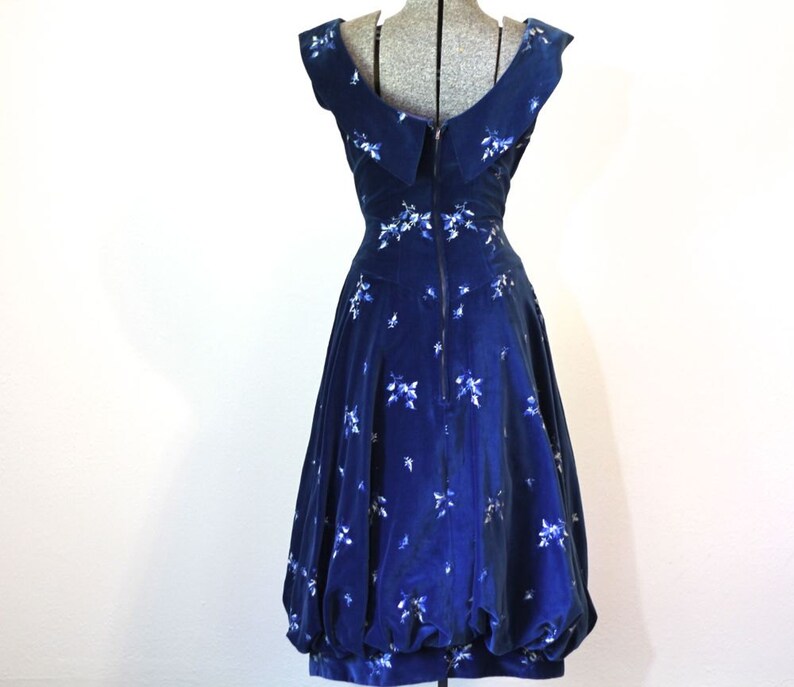 Puede incluir: Un vestido de terciopelo azul con estampado floral blanco y escote de pico. El vestido tiene un corpi&ntilde;o ajustado y una falda completa.