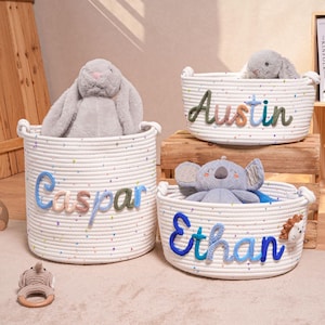 Könnte beinhalten: Drei weiße Seilkörbe mit bunten Sprenkeln und personalisierten Namen: "Caspar", "Austin" und "Ethan". Jeder Korb enthält ein Plüschtier. Der "Caspar"-Korb ist rund, die anderen sind oval. Ein Holzregal und Spielzeug sind im Hintergrund.
