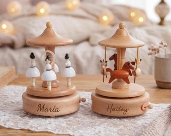 May include: Two wooden music boxes with light wood bases. The left music box features three white-clad ballerinas and is engraved with the name Maria. The right music box features three small horses and is engraved with the name Hailey.