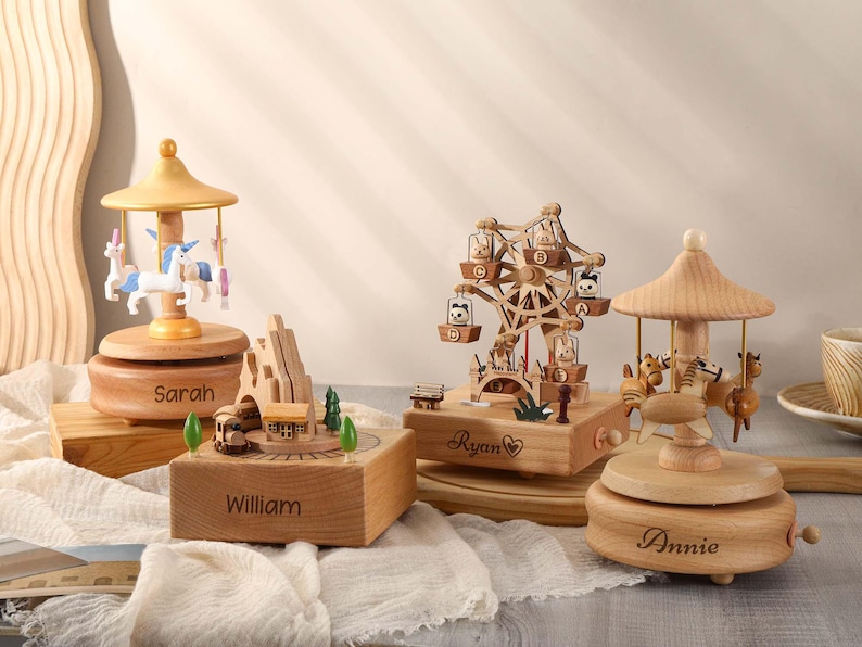 May include: Four wooden music boxes with different themes. The first music box features a carousel with unicorns and is engraved with the name "Sarah". The second music box features a train and is engraved with the name "William". The third music box features a Ferris wheel and is engraved with the name "Ryan". The fourth music box features a carousel with horses and is engraved with the name "Annie".
