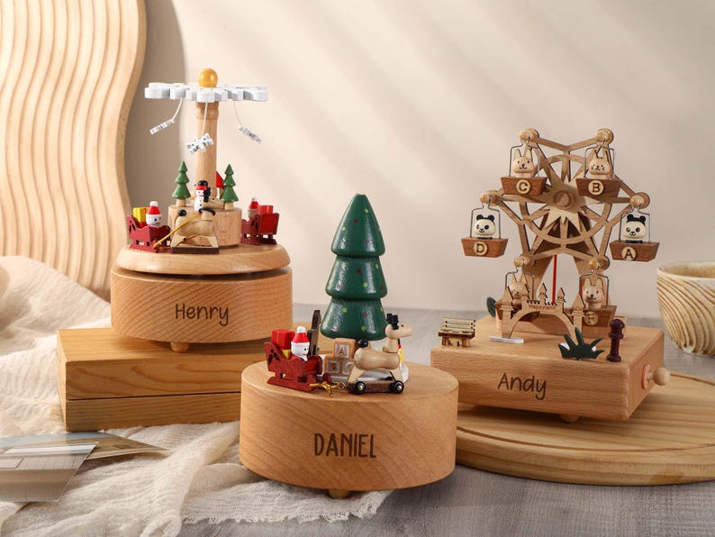 May include: Three wooden music boxes with different designs. The first music box features a carousel with a snowman and reindeer. The second music box features a Christmas tree with a reindeer and Santa Claus. The third music box features a Ferris wheel with animals. Each music box has a personalized name on the base: Henry, Daniel, and Andy.